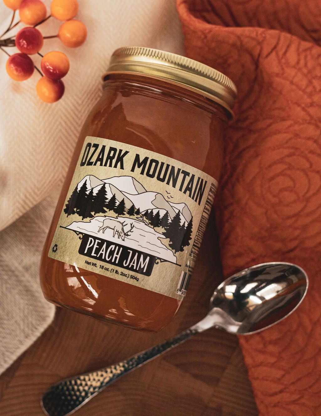 A jar of Ozark Mountain Peach Jam on a wooden board with a spoon