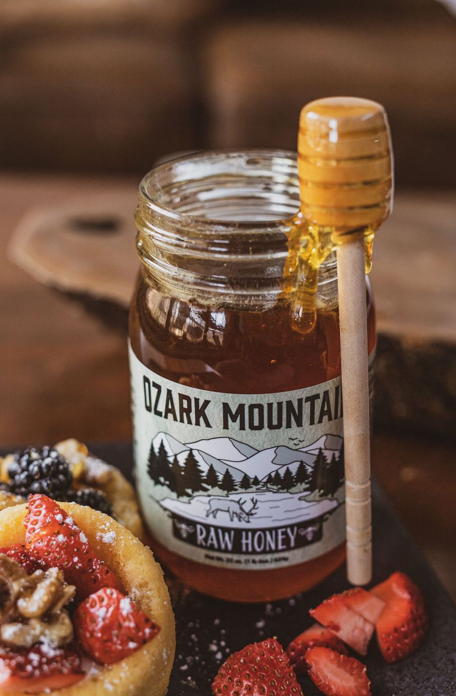 A jar of Ozark Mountain Raw Honey with a wooden honey dipper