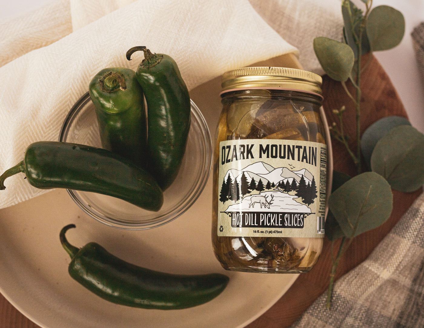 A jar of Ozark Mountain Hot Dill Pickle Slices beside fresh jalapeños
